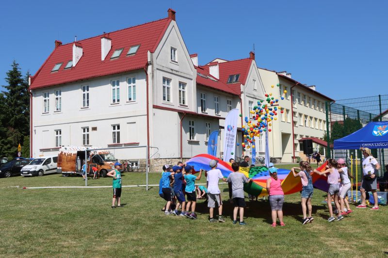 Dzieci bawią się kolorowymi kulkami. W tle Szkoła Podstawowa w Albigowej